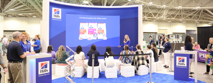 attendees sitting at exhibitor booth listening to presentation